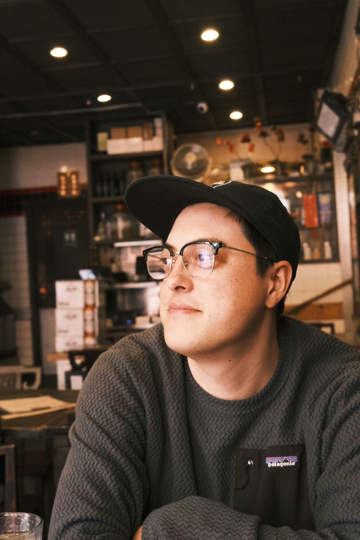 Austin John Smith, in a ball cap and glasses, looking off-frame in warm light.