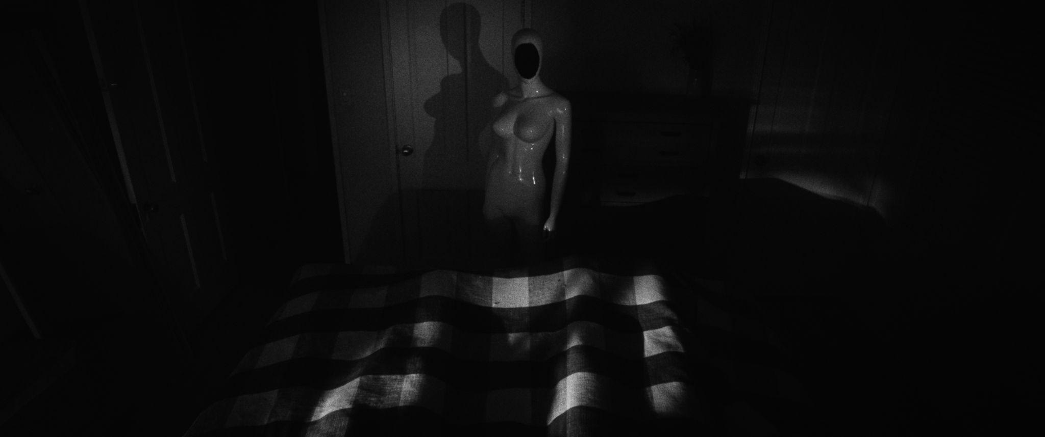 A pale figure stands at the foot of a bed striped with window light.
