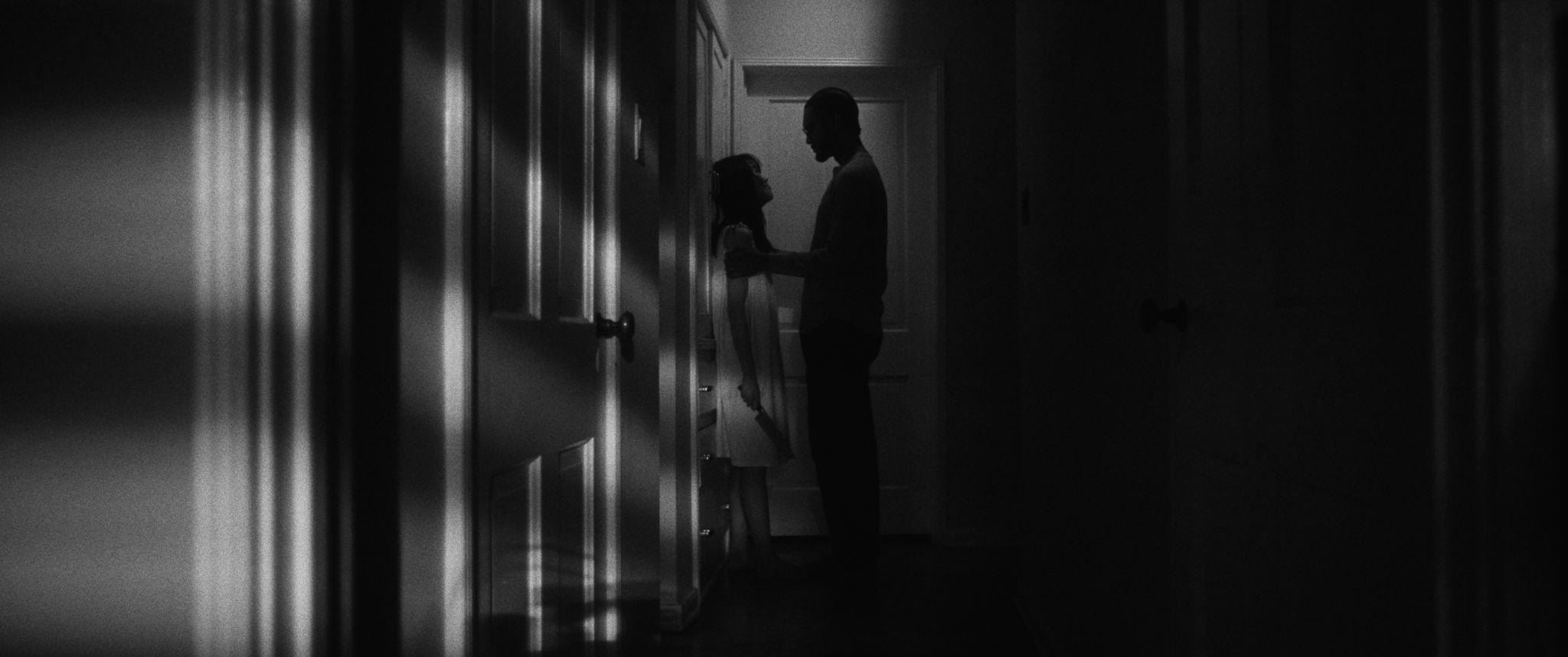 Jane and Frank stand apart in a dark hallway, lit by a single doorway.