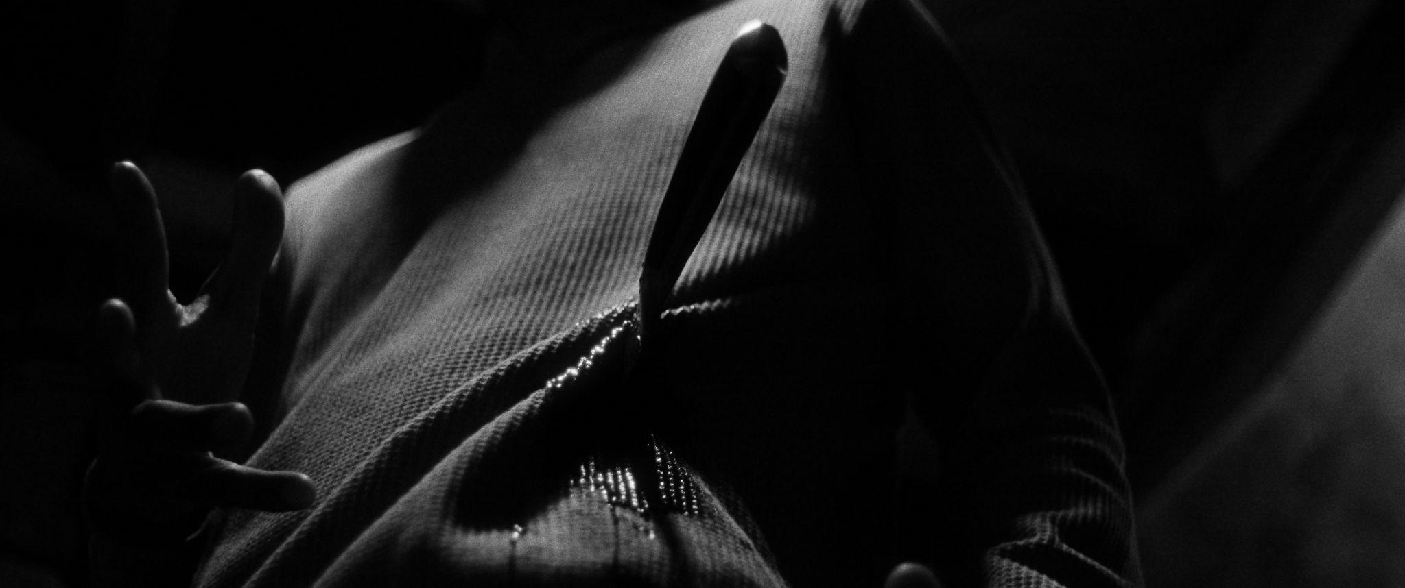 A kitchen knife pressed against a chest in hard light.
