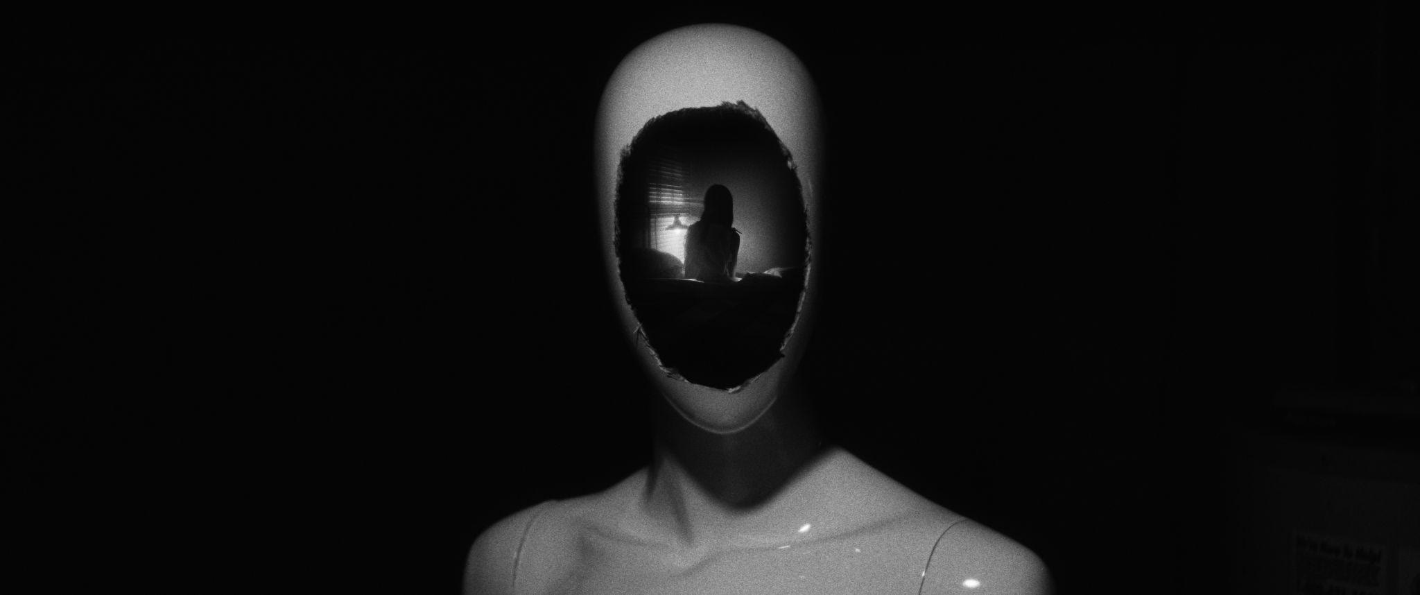 The mannequin's torn face frames a distant bedroom where Jane sits.